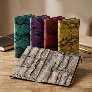 May include: A collection of five long wallets featuring a snakeskin pattern. Four wallets stand upright in teal, purple, red, and yellow, while one wallet lies open in the foreground, displaying a beige and black snakeskin print with card slots.