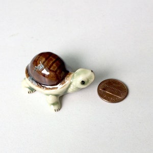 May include: A small ceramic turtle figurine with a brown shell and a light green body. The turtle is about the size of a US penny.