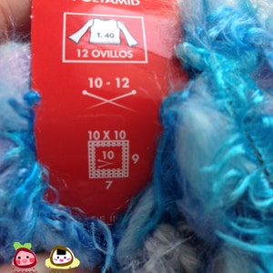May include: A red label with white text that reads "15% Poliam Polyamide Polyamid" and "T. 40 12 Ovillos 10-12 10 x 10 10 9 7 FIN". The label is attached to a skein of blue and white yarn.