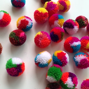 May include: A collection of colorful pom poms in various shades of red, orange, yellow, green, blue, purple, and white. The pom poms are made of yarn and are soft and fluffy.
