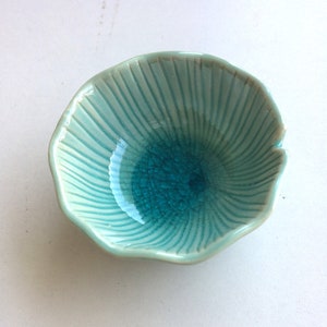 Könnte beinhalten: Eine kleine, tealblaue Keramikschale mit geriffeltem Rand und einer craquelé-Glasur.