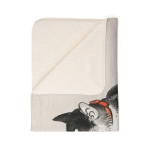 May include: A soft, plush throw blanket with a black and white cat illustration on one side and a white sherpa fleece on the other side. The cat is looking to the left and has a red bow on its head.