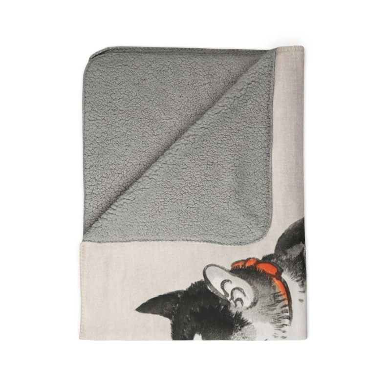 May include: A soft, gray fleece blanket with a white and black cat illustration on one side. The cat is looking to the left and has a red bow around its neck.