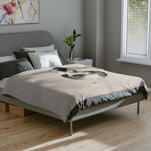 May include: A gray bed with a white and gray patterned duvet cover featuring a black and white ink drawing of a cat. The bed has a gray headboard and a black and gray footboard.