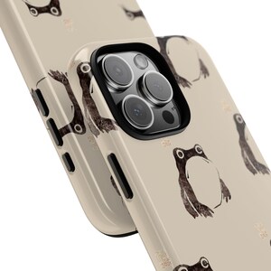 May include: Beige phone case featuring a repeating pattern of stylized brown frog illustrations. The case has a black camera lens border and a glossy finish. The design includes Japanese text accents.
