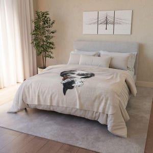 May include: A beige fleece throw blanket with a black and white cat illustration. The cat is curled up and sleeping with its head resting on its paws. The blanket is on a bed with white bedding and pillows.