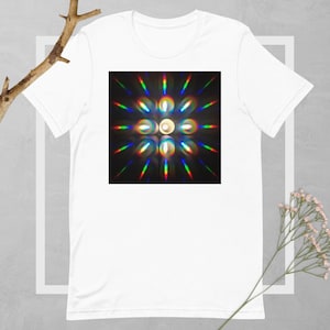 Pode incluir: Uma camiseta branca com um design abstrato colorido na frente. O design apresenta um círculo branco central rodeado por um anel de círculos menores, todos irradiando para fora com linhas de cores do arco-íris.
