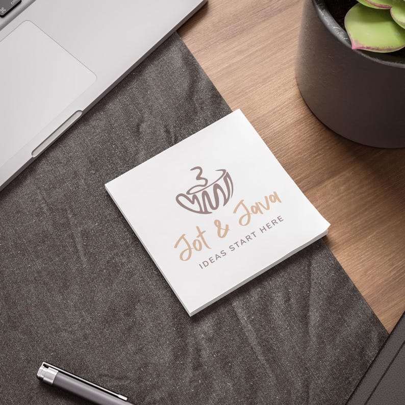 Puede incluir: Un bloc de notas adhesivas blancas con el texto "Jot & Java IDEAS START HERE" en marr&oacute;n y beige, y un logotipo de taza de caf&eacute;. Las notas est&aacute;n sobre una superficie gris oscura, junto a un port&aacute;til y un bol&iacute;grafo.