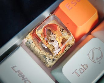 May include: A clear resin keycap with a red and orange abstract design. The keycap is on a white keyboard with the keys "Esc" and "Tab" visible.