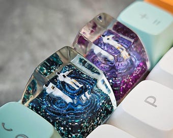 Peut inclure: Deux touches de clavier en résine transparente avec des paillettes incrustées. Une touche de clavier a un tourbillon de paillettes bleu et vert avec des figures blanches à l'intérieur. L'autre touche de clavier a un tourbillon de paillettes violettes avec des figures blanches à l'intérieur.