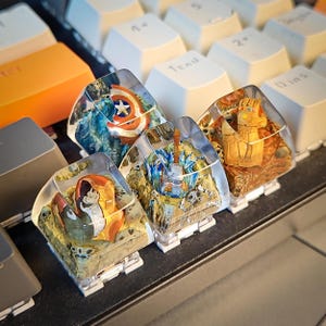 May include: Four clear resin keycaps with different superhero themed designs. The keycaps feature Captain America, Thor, Iron Man, and Thanos. The keycaps are on a keyboard.