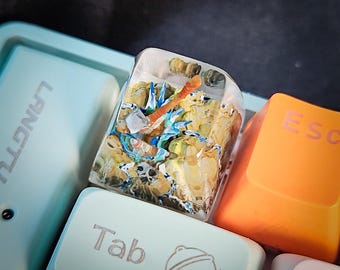 May include: A clear resin keycap with a colorful, detailed miniature scene inside. The scene features a blue and white creature with a red and orange object. The keycap is labeled "Tab" and is surrounded by other keyboard keys.