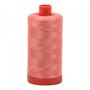 May include: A spool of coral-coloured sewing thread wound tightly around a cylindrical core. The spool features a bright orange-red plastic top and base, with the embossed text AURIFIL visible along the bottom edge of the plastic base.