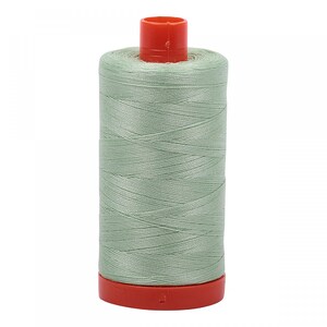 Puede incluir: Una bobina de hilo de coser verde claro con una bobina de plástico roja.