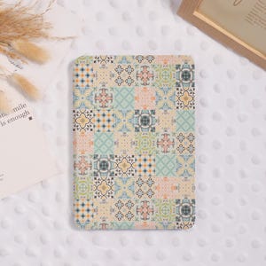 May include: A rectangular item with a patchwork design. The design features squares with floral and geometric patterns in beige, blue, orange, and green. The item is on a white, textured surface.