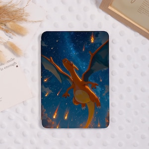 May include: A tablet case with a colourful illustration of Charizard, an orange dragon, flying through a starry night sky with falling meteors. The case has a glossy finish and a protective design.