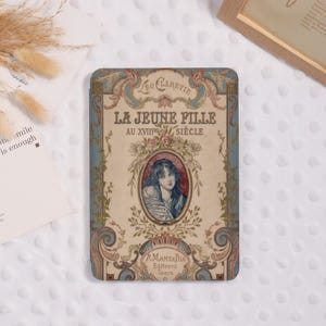 May include: A rectangular case with an antique design. The case features the text "LA JEUNE FILLE AU XVIIIe SIÈCLE" and an illustration of a woman. The case has a blue and beige color scheme with floral accents.