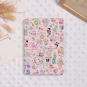 Könnte beinhalten: Eine rosa Tablet-Hülle mit bunten Cartoon-Illustrationen von Tieren, Herzen, Schleifen und Blumen. Die Hülle hat ein sich wiederholendes Muster aus niedlichen Figuren und dekorativen Elementen.