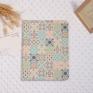 Peut inclure: Une housse de tablette rectangulaire présentant une grille répétitive de carreaux carrés aux motifs et couleurs variés, incluant des nuances de bleu, orange, vert et crème. Le design imite le carrelage traditionnel avec des motifs géométriques.