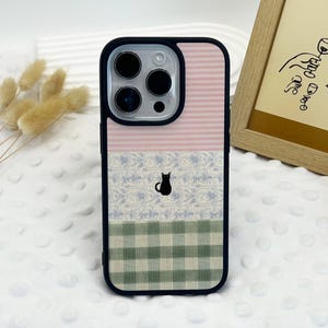 May include: A decorative phone case with a black border. The case features a pink and white striped top section, a middle section with a blue floral pattern and a black cat silhouette, and a green and white checkered bottom section.