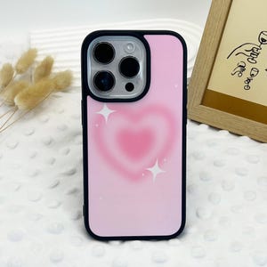 May include: A pink phone case with a heart design and white stars. The case is black and has a cutout for the camera.
