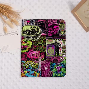 May include: A rectangular tablet case featuring a vibrant collage of neon-coloured graphics, including multiple skulls, a cross, a creature, and the text "I LOVE ME" and "JUICY COUTURE EXILE." The design incorporates bright pink, green, and black patterns.