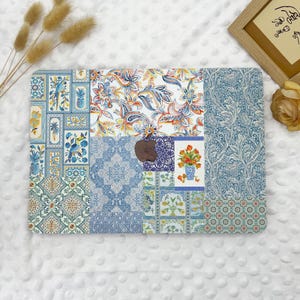 May include: A decorative laptop skin featuring a patchwork design with various patterns. The patterns include floral, paisley, and geometric motifs in shades of blue, white, orange, and green. The skin has a cutout for the Apple logo.