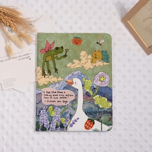 Könnte beinhalten: Ein farbenfrohes Notizbuch mit einer skurrilen Illustration mit einer Gans, Fröschen und einer Biene. Das Cover hat ein Zitat von Vincent van Gogh. Das Design umfasst einen grünen Hintergrund mit Bergen, Wolken und Blumen.