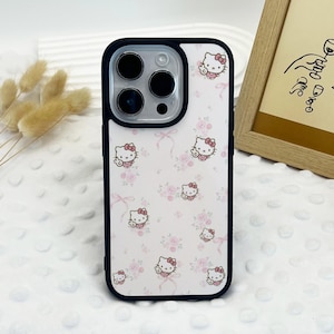May include: A white phone case with a black border and a pattern of Hello Kitty characters and pink flowers.