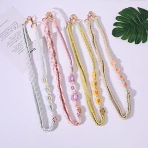 May include: Six colorful, braided purse straps with gold-colored clasps. The straps are in pastel colors, including blue, pink, yellow, and green. Some straps feature decorative flower accents. The straps are designed for use with handbags or other accessories.