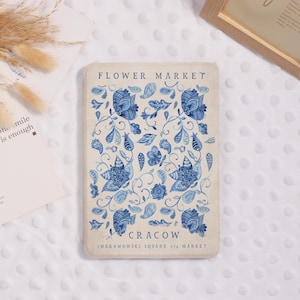Könnte beinhalten: Eine rechteckige cremefarbene Hülle mit blauem Blumenmuster. Die Hülle zeigt oben den Text "FLOWER MARKET" und unten "CRACOW", mit zusätzlichem Text darunter. Das Blumenmuster umfasst stilisierte Blumen und Blätter.