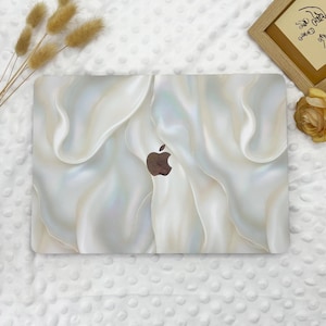 May include: A white laptop skin with a pearlescent, iridescent, and textured design. The skin features a subtle, swirling pattern that resembles flowing fabric. The Apple logo is visible in the centre of the skin.