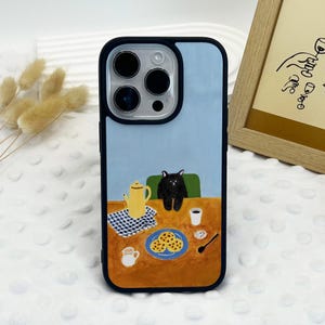 May include: A black phone case with a blue background and a cartoon illustration of a black cat sitting at a table with a teapot, cookies, and a cup of coffee.
