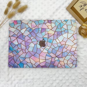 May include: A laptop cover with a stained glass design in shades of blue, purple, pink, and white. The cover features a brown Apple logo in the center. The design is made up of irregular shapes separated by brown lines.