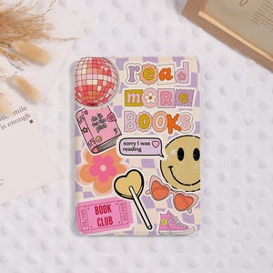 May include: A decorative phone case with a checkerboard pattern in lavender and cream. The case features stickers with the words "read more books", a disco ball, a smiley face, a book, and a pair of heart-shaped sunglasses.