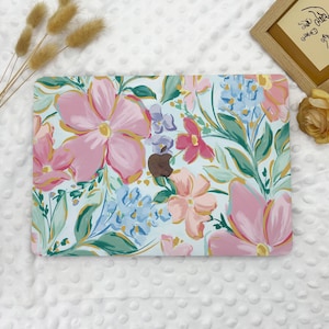 May include: A white laptop case with a floral design featuring pink, blue, and green flowers on a white background. The case has a gold apple logo in the center.