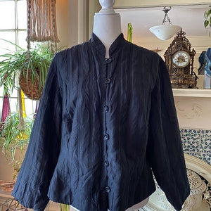 Puede incluir: Una chaqueta acolchada negra con cuello mandar&iacute;n y cierre de botones. La chaqueta tiene una silueta ligeramente ajustada y mangas largas.