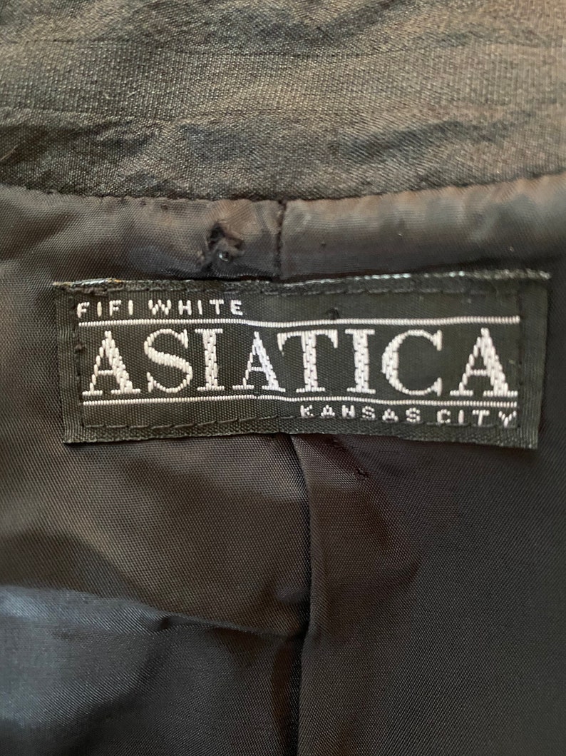 Puede incluir: Una etiqueta negra con texto blanco que dice "Fifi White Asiatica Kansas City".