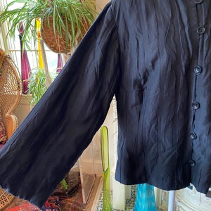 Puede incluir: Una camisa negra de manga larga con cuello mandar&iacute;n y tejido texturizado y arrugado.