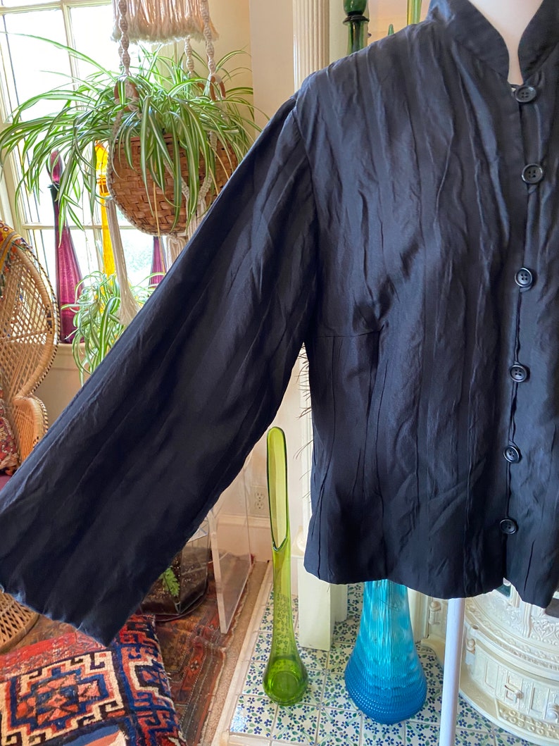 Puede incluir: Una camisa negra de manga larga con cuello mandar&iacute;n y tejido texturizado y arrugado.