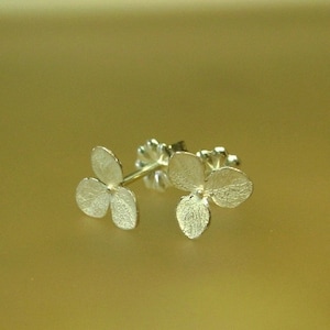 May include: A pair of silver earrings shaped like hydrangea flowers. The earrings are delicate and have a textured surface.