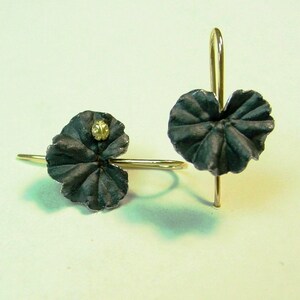 May include: A pair of silver earrings with a black finish. Each earring features a small, round, gold-colored accent in the center of a leaf-shaped design.