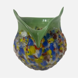 May include: A green glass owl vase with a colorful, speckled design. The owl's eyes are made of clear glass with a red and yellow center.
