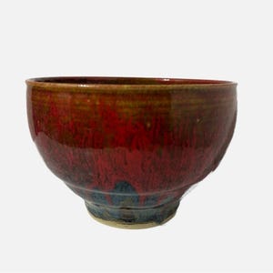 May include: A round ceramic bowl featuring a glossy glaze with a vibrant red centre that transitions into deep brown and dark blue tones near the base. The bowl has a smooth, curved silhouette with a wide opening and a narrow, sturdy circular foot.