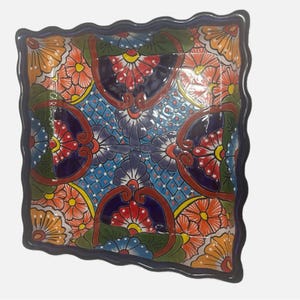 Puede incluir: Un plato cuadrado de cerámica con un borde festoneado. El plato está decorado con un colorido patrón floral en tonos de azul, rojo, naranja, amarillo y verde.