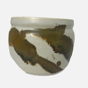 May include: A white ceramic bowl with brown and green glaze. The glaze has a streaky, abstract pattern.