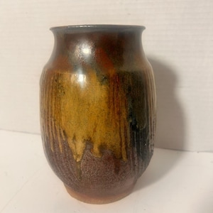 May include: A ceramic vase with a rounded body and a flared rim. The surface features a reactive glaze with blended tones of deep brown, ochre, and golden yellow, characterised by vertical drip patterns and a textured, mottled finish throughout.