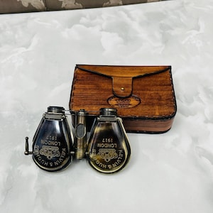 May include: Antique brass and black binoculars with a leather case. The binoculars are engraved with "KELVIN & HUGH LONDON 1917". The leather case is brown with a flap closure.