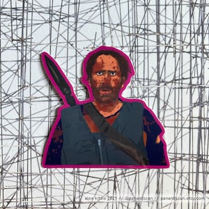 May include: A sticker featuring a close-up portrait of a man with a beard and blood splatters on his face. He is wearing a dark blue vest with a strap and a large knife is strapped to his back. The sticker has a pink border.