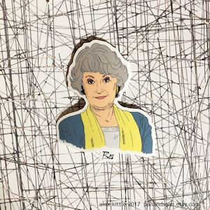 May include: A sticker featuring a cartoon illustration of a woman with gray hair, wearing a blue jacket and yellow scarf. The sticker has the name "Bea" written on it. The background is a white surface with a black linear design.